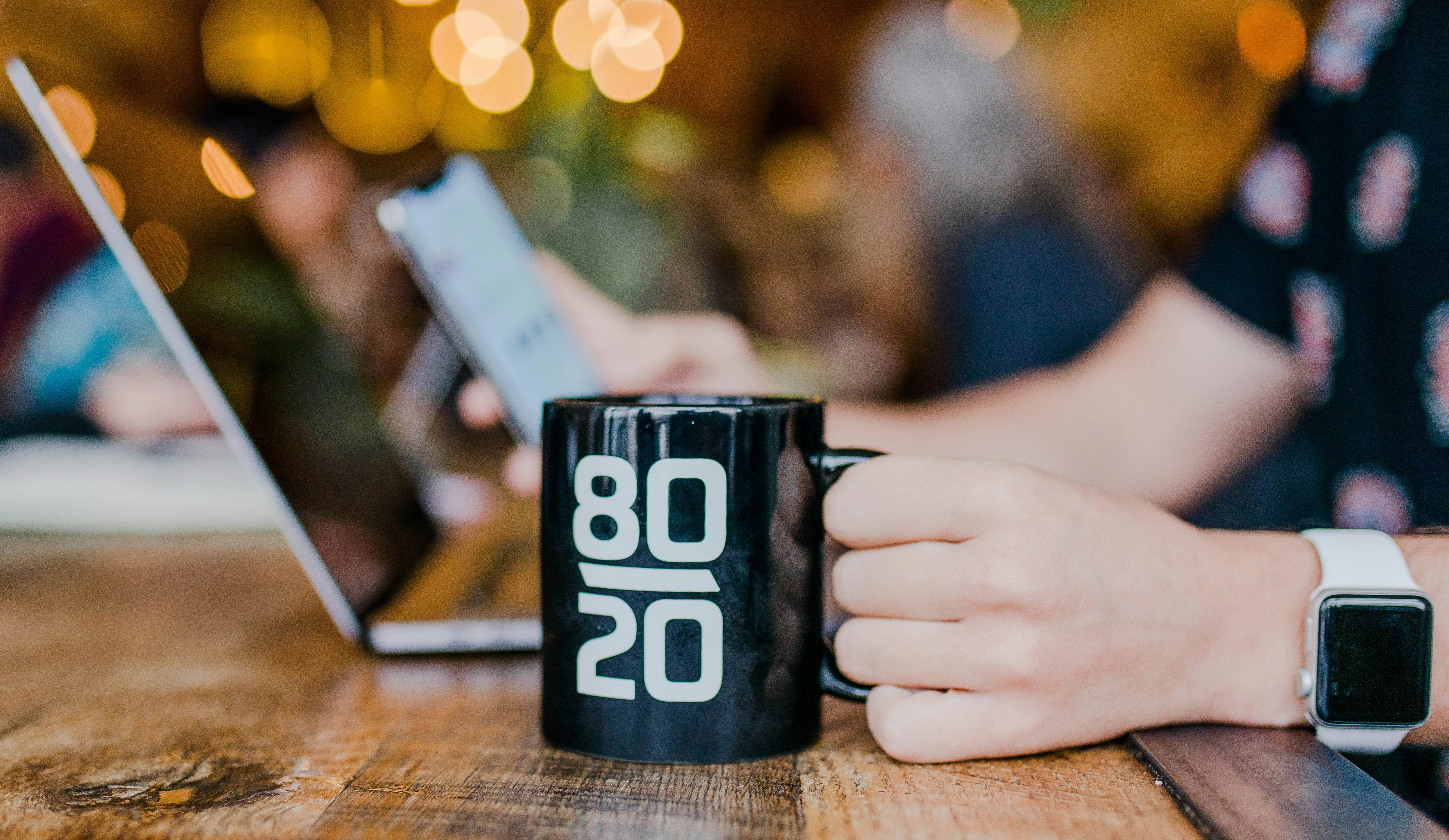 A black mug with the numbers 80 and 20 written on it, on a desk with a computer